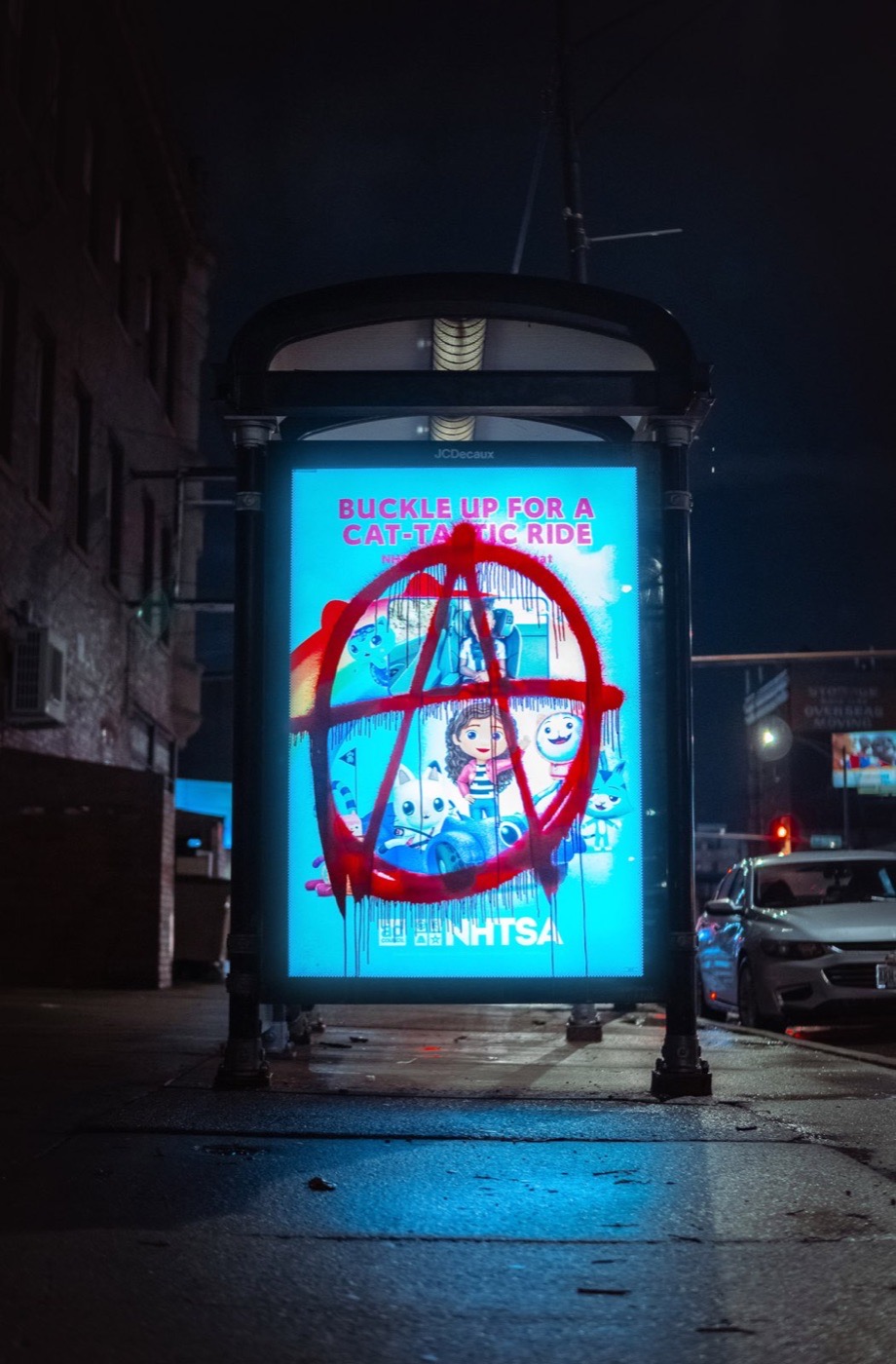 Bus shelter advertisement at night covered in red graffiti and glowing blue light
