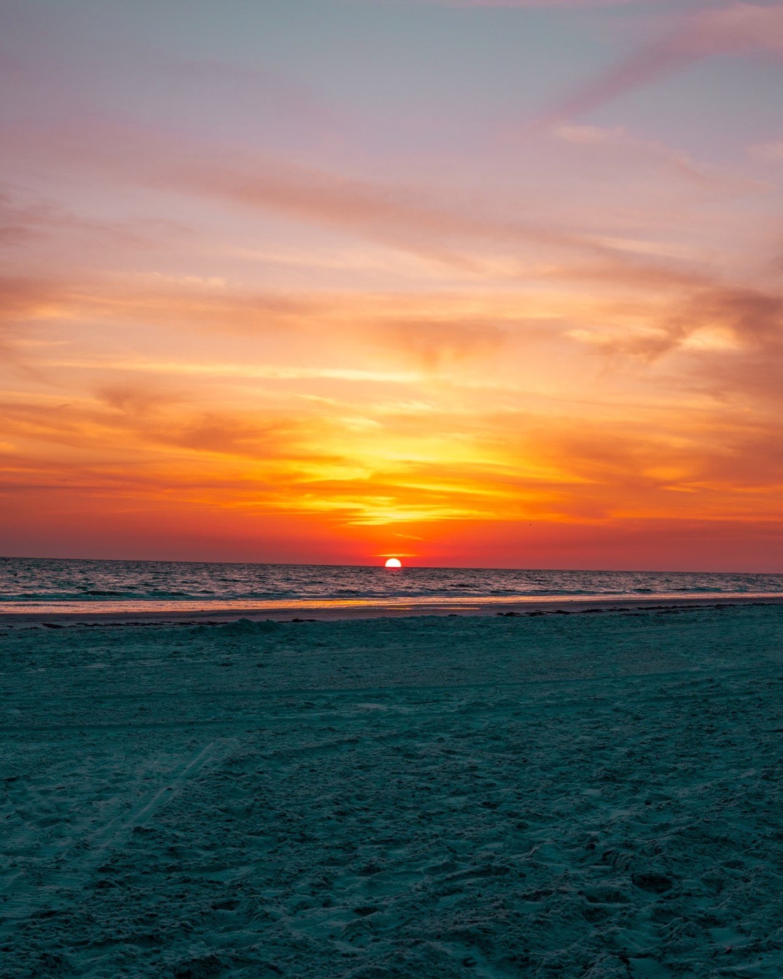 Sun setting over a beach with orange and pink light across the sky