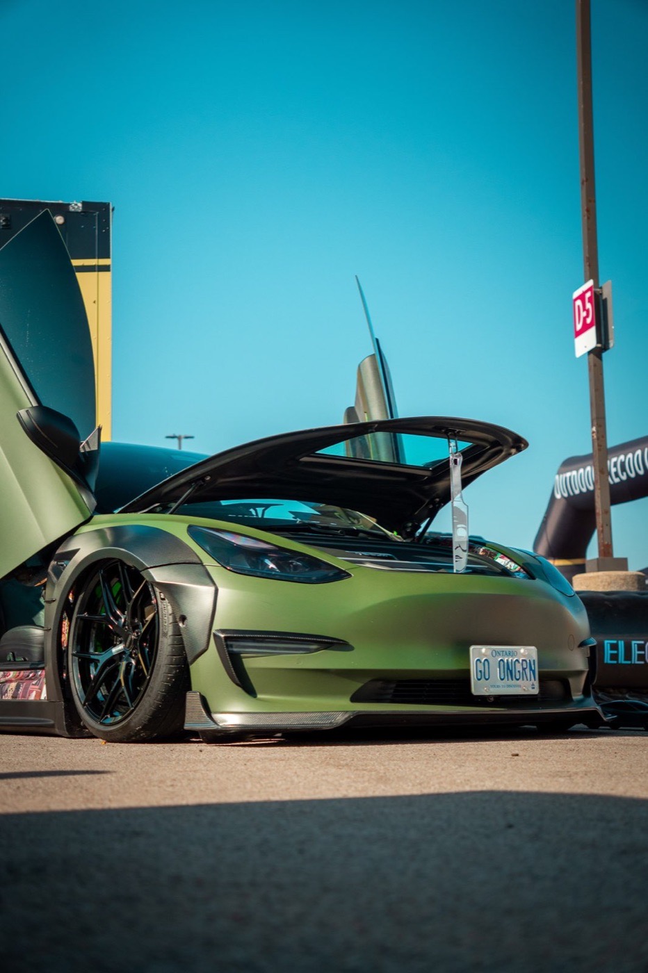 Low-angle photograph of a matte green custom car at an outdoor show