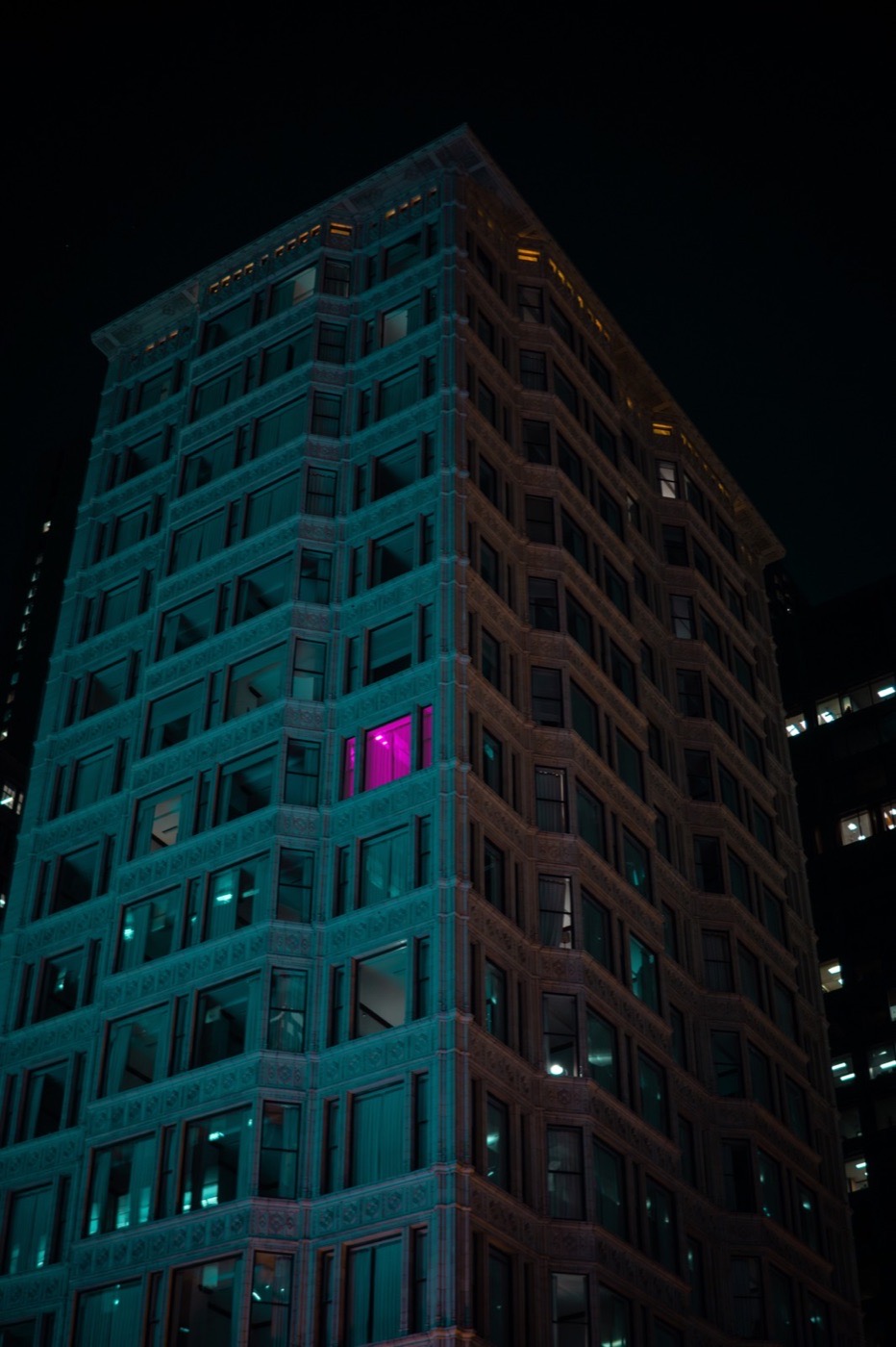 Tall building at night with a single magenta-lit window
