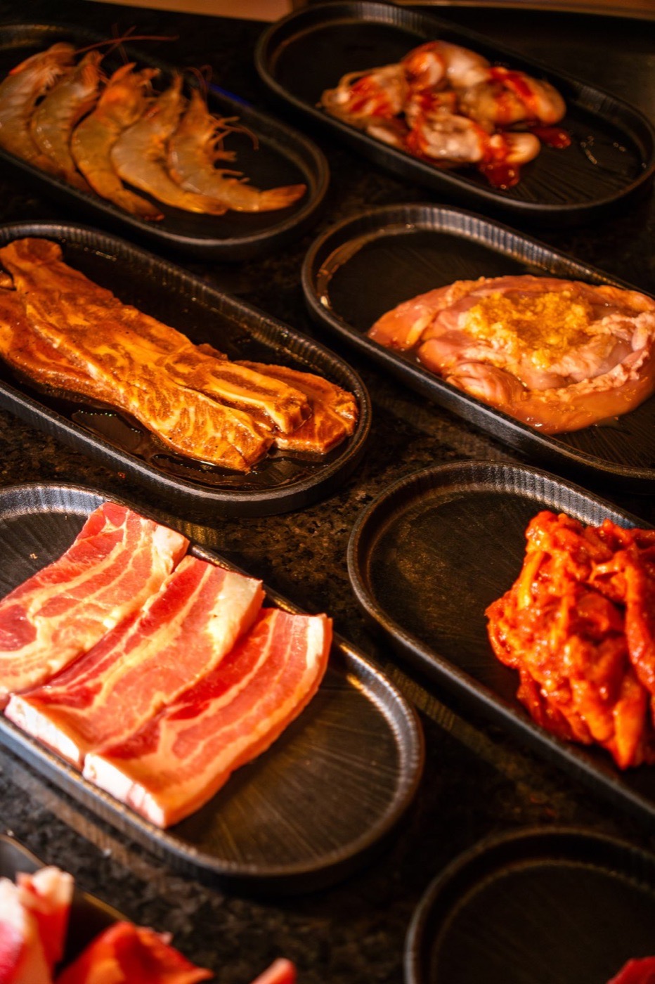 Table filled with plates of raw meat and seafood in warm restaurant lighting